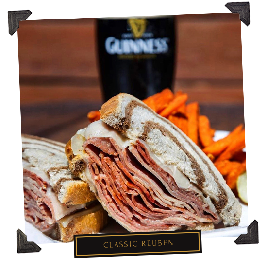 Reuben sandwich cut in half with sweet potato fries and a glass of Guinness